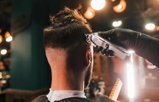 vue rapprochée d'un jeune homme barbu assis et se faisant couper les cheveux dans un salon de coiffure photo