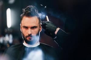 jeune homme barbu assis et se coupe les cheveux dans un salon de coiffure photo