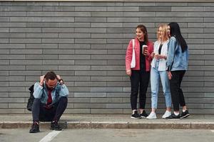 trois femmes debout et riant du gars assis à l'extérieur près du bâtiment pendant la journée photo