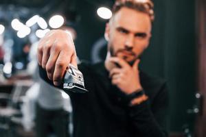 jeune homme barbu debout dans un salon de coiffure et tenant une tondeuse photo