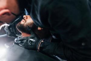 jeune homme avec une coiffure élégante assis et se rasant la barbe dans un salon de coiffure photo