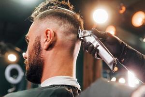 vue rapprochée d'un jeune homme barbu assis et se faisant couper les cheveux dans un salon de coiffure photo
