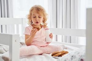 prendre un petit déjeuner en mangeant des biscuits. jolie petite fille en vêtements décontractés est à l'intérieur à la maison pendant la journée photo