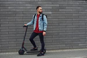 vue latérale d'un beau jeune homme en vêtements décontractés qui fait du scooter électrique à l'extérieur pendant la journée ensoleillée photo