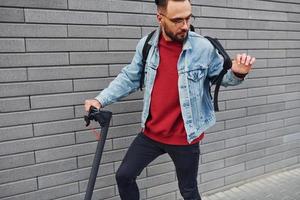 vue latérale d'un beau jeune homme en vêtements décontractés qui fait du scooter électrique à l'extérieur pendant la journée ensoleillée photo