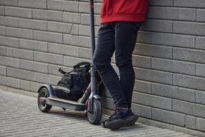 vue rapprochée d'un gars dans des vêtements décontractés qui se tient debout avec un scooter électrique à l'extérieur pendant la journée ensoleillée photo