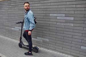 beau jeune homme en vêtements décontractés debout avec un scooter électrique à l'extérieur pendant la journée ensoleillée photo