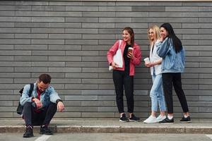 trois femmes debout et riant du gars assis à l'extérieur près du bâtiment pendant la journée photo