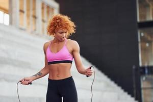 jeune femme rousse européenne en vêtements sportifs sautant avec une corde à l'extérieur photo