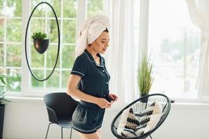 joyeuse jeune femme en pyjama et serviette blanche sur la tête debout à l'intérieur pendant la journée photo