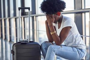 triste et déprimée, une jeune passagère afro-américaine en vêtements décontractés est à l'aéroport avec des bagages photo