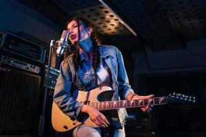 jeune belle interprète féminine avec guitare chantant et répétant dans un studio d'enregistrement photo