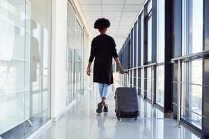 vue arrière d'une jeune passagère afro-américaine en vêtements décontractés qui se trouve à l'aéroport avec des bagages photo