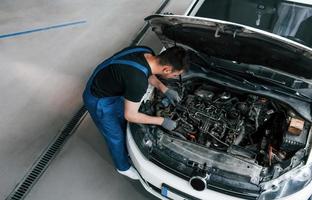 sous la capuche. un homme en uniforme de travail répare une automobile blanche à l'intérieur. conception de service automobile photo