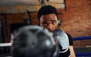 un boxeur afro-américain fort en vêtements sportifs s'entraîne dans la salle de sport photo