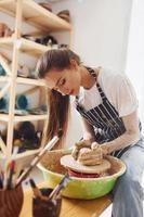 jeune femme céramiste travaillant en utilisant un tour de potier à l'intérieur et en fabriquant un produit en argile fait main photo