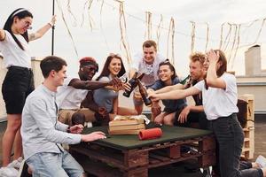 avec de délicieuses pizzas. un groupe de jeunes en vêtements décontractés fait la fête ensemble sur le toit pendant la journée photo