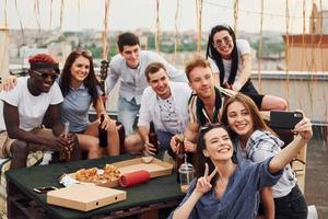 fille faisant selfie. avec de délicieuses pizzas. un groupe de jeunes en vêtements décontractés fait la fête ensemble sur le toit pendant la journée photo