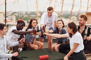 avec de délicieuses pizzas. un groupe de jeunes en vêtements décontractés fait la fête ensemble sur le toit pendant la journée photo