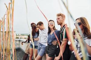 appuyé sur le bord du toit avec décore. un groupe de jeunes en vêtements décontractés fait la fête ensemble pendant la journée photo