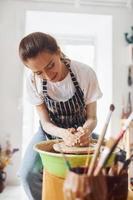 jeune femme céramiste travaillant en utilisant un tour de potier à l'intérieur et en fabriquant un produit en argile fait main photo