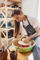 jeune femme céramiste travaillant en utilisant un tour de potier à l'intérieur et en fabriquant un produit en argile fait main photo