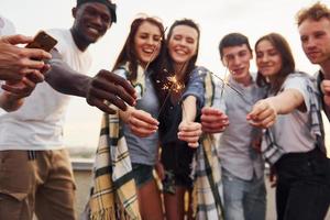 avec des cierges magiques dans les mains. un groupe de jeunes en vêtements décontractés fait la fête ensemble sur le toit pendant la journée photo