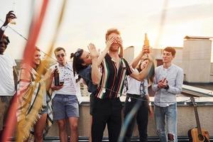 jouer à un jeu. les yeux de l'homme couverts par les mains. un groupe de jeunes en vêtements décontractés fait la fête ensemble sur le toit pendant la journée photo