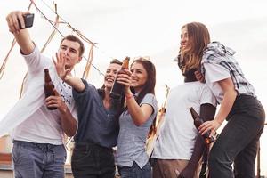 debout ensemble et prenant selfie. un groupe de jeunes en vêtements décontractés fait la fête ensemble sur le toit pendant la journée photo