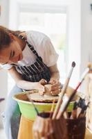 jeune femme céramiste travaillant en utilisant un tour de potier à l'intérieur et en fabriquant un produit en argile fait main photo