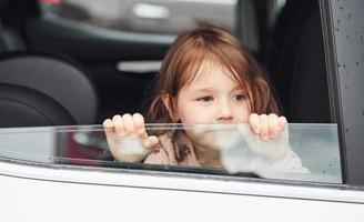 jolie petite fille regarde à travers la fenêtre de la voiture. conception du voyage et des vacances photo