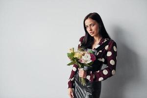 belle jeune brune en jupe noire debout à l'intérieur sur fond blanc avec bouquet dans les mains photo