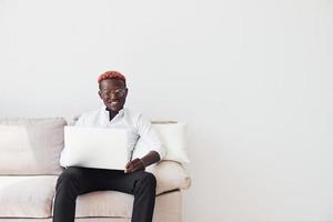 jeune homme afro-américain en vêtements formels assis à l'intérieur avec un ordinateur portable dans les mains photo