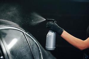 pulvériser le véhicule. une automobile noire moderne est nettoyée par une femme à l'intérieur d'une station de lavage de voiture photo