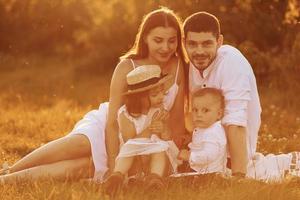 assis sur l'herbe. père, mère avec fille et fils passant du temps libre à l'extérieur aux beaux jours de l'été photo