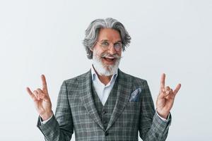 dans des vêtements élégants. debout contre le mur blanc. homme moderne et élégant aux cheveux gris et à la barbe à l'intérieur photo