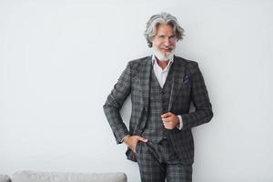 dans des vêtements élégants. debout contre le mur blanc. homme moderne et élégant aux cheveux gris et à la barbe à l'intérieur photo