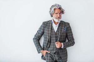 dans des vêtements élégants. debout contre le mur blanc. homme moderne et élégant aux cheveux gris et à la barbe à l'intérieur photo