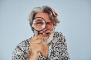 s'amuser avec une loupe. homme moderne et élégant aux cheveux gris et à la barbe à l'intérieur photo