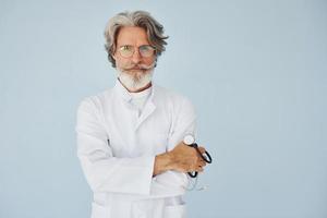 médecin en blouse blanche contre le mur. homme moderne et élégant aux cheveux gris et à la barbe à l'intérieur photo