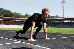 le coureur est en position de départ sur la piste. jeune homme sportif en chemise noire et pantalon à l'extérieur pendant la journée photo