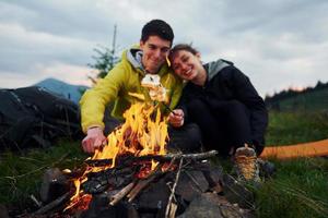 couple avec guimauve près du feu de camp. majestueuses montagnes des carpates. beau paysage de nature intacte photo