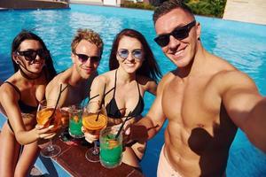 faire des selfies. un groupe de jeunes gens heureux s'amuse dans la piscine pendant la journée photo