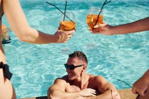 cocktails frais dans les mains. un groupe de jeunes gens heureux s'amuse dans la piscine pendant la journée photo