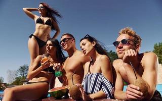 temps chaud et ensoleillé. un groupe de jeunes gens heureux s'amuse dans la piscine pendant la journée photo