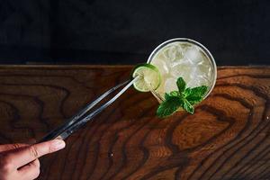 la main du serveur. menthe verte et citron jaune. vue rapprochée du cocktail d'été frais sur la table en bois photo