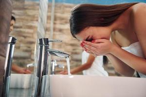 belle jeune femme debout dans la salle de bain près du miroir et se lavant le visage. amis derrière photo