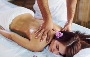 fleur violette couchée. l'homme fait un massage à la jeune femme en serviette blanche à l'intérieur photo