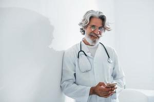 médecin senior aux cheveux gris et à la barbe en blouse blanche est à l'intérieur de la clinique photo