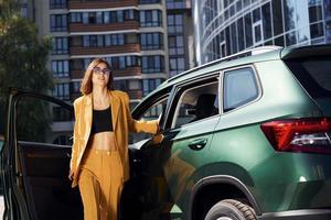 marche en avant de l'automobile. jeune femme à la mode en manteau de couleur bordeaux pendant la journée avec sa voiture photo